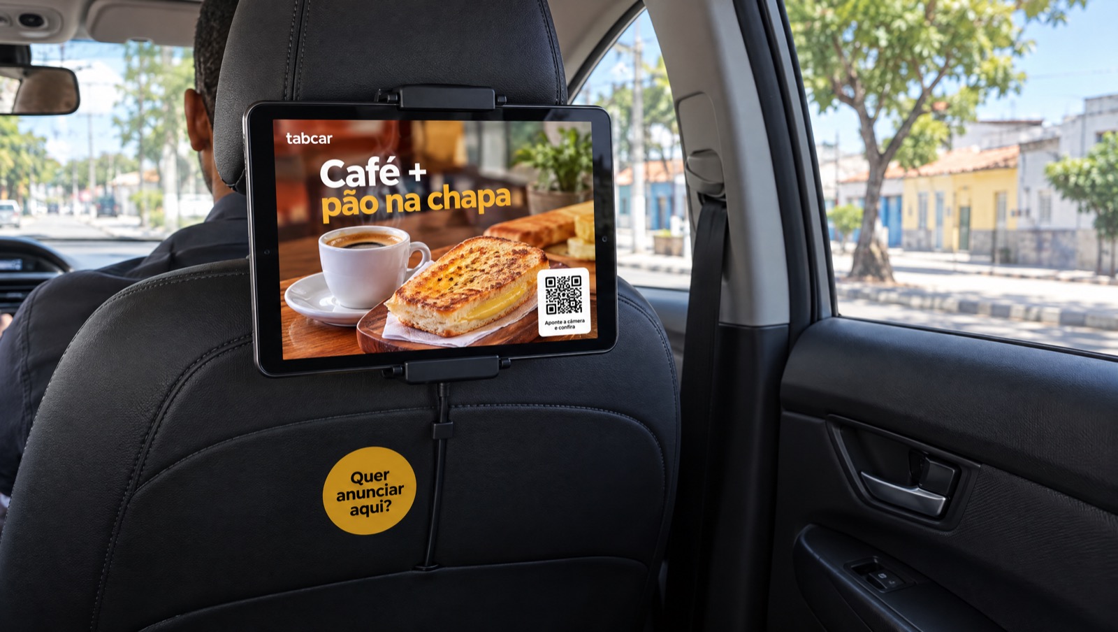 Tablet da tabcar instalado no encosto do banco do motorista, mostrando o anúncio de uma padaria com QR code